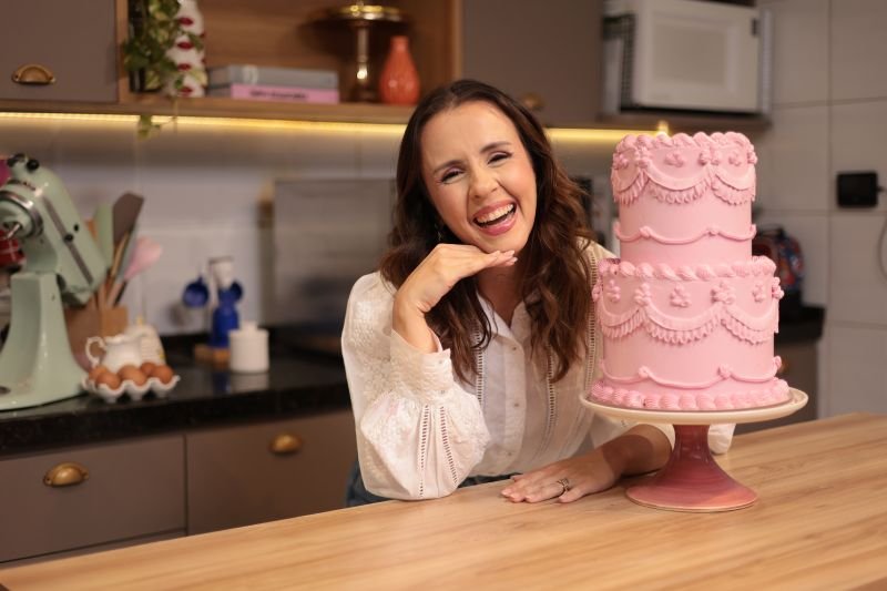 Carol Pinho, instrutora da Docearte, sorrindo ao lado de um bolo rosa decorado